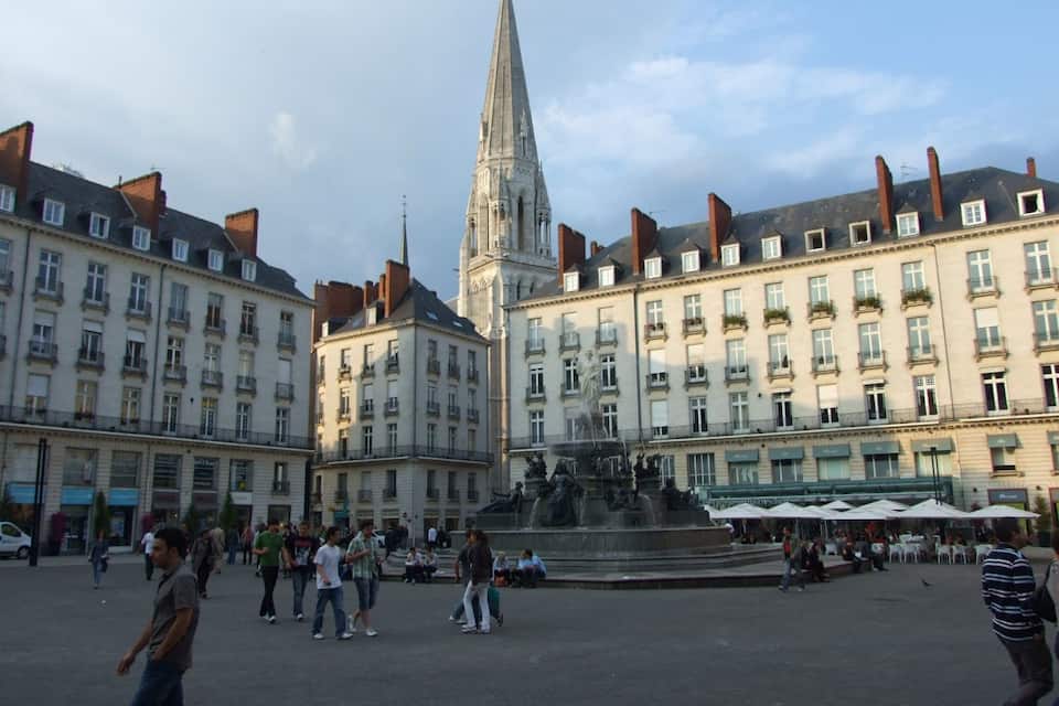 A historic square with a prominent church spire, a fountain, and surrounding buildings with balconies.
