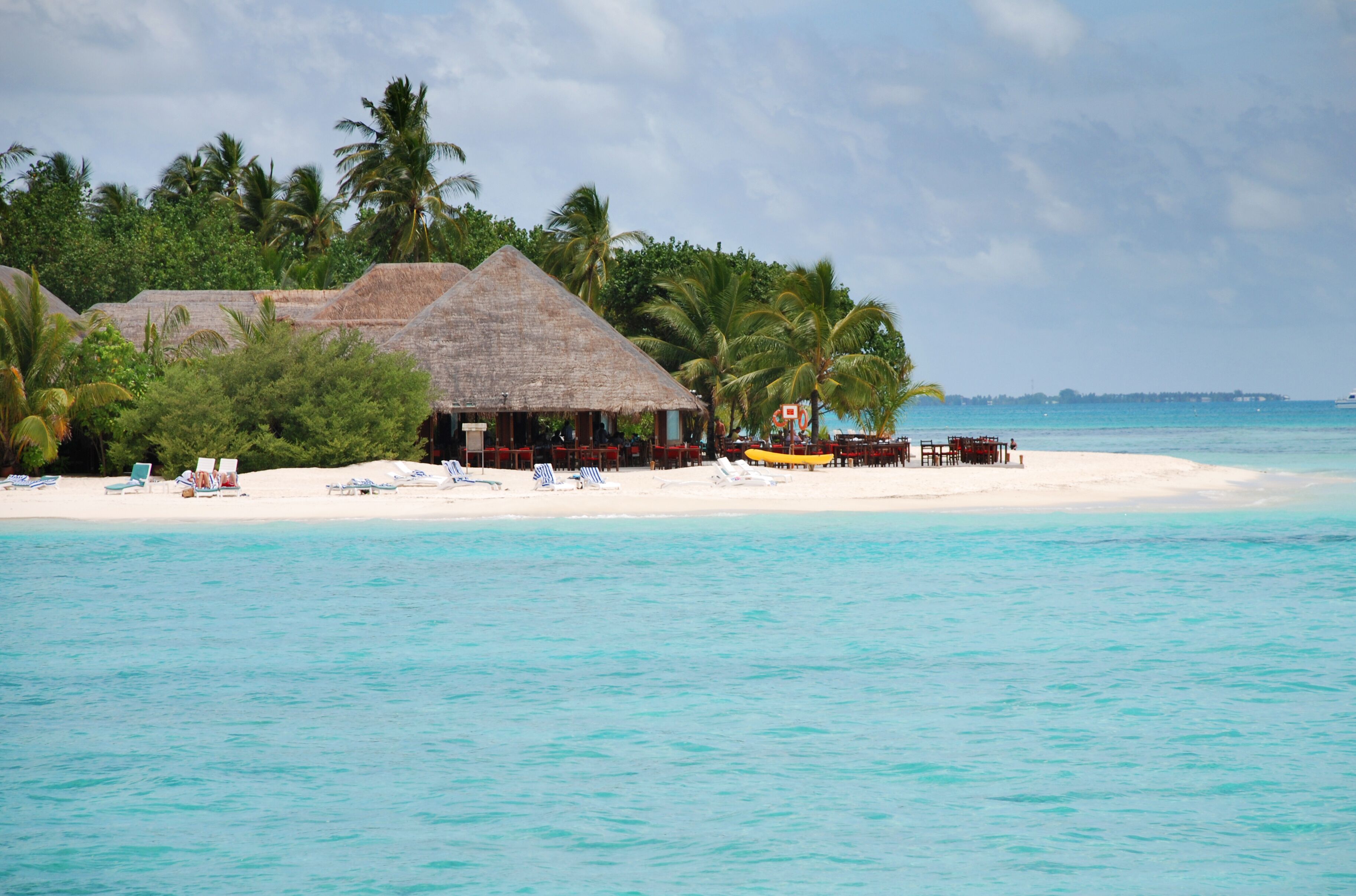 A beach with thatched-roof huts, palm trees, and white sand.