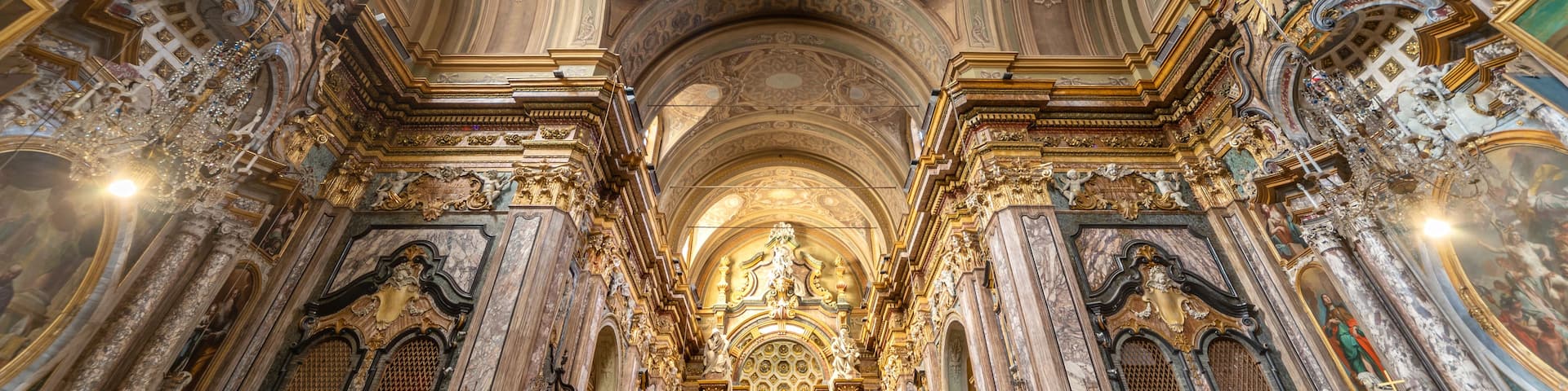 An ornate church interior with detailed frescoes, marble columns, and a large central altar.