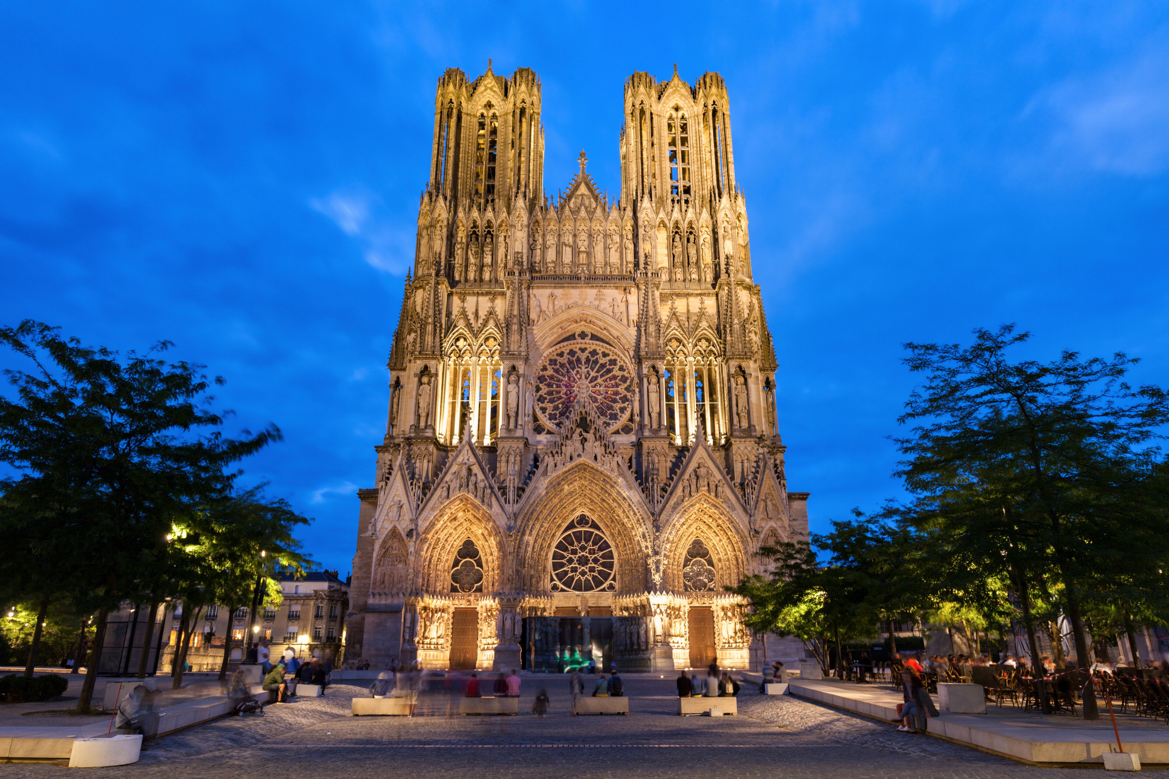 Una catedral gótica con dos torres gemelas, un gran rosetón y un patio con zonas de estar.