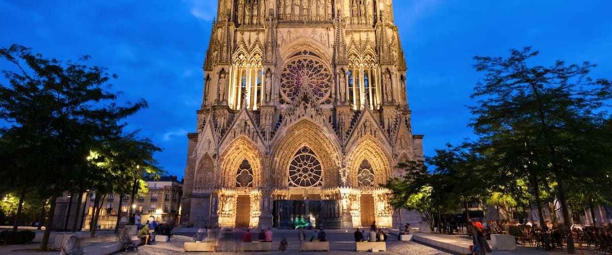 Una catedral gótica con dos torres gemelas, un gran rosetón y un patio con zonas de estar.