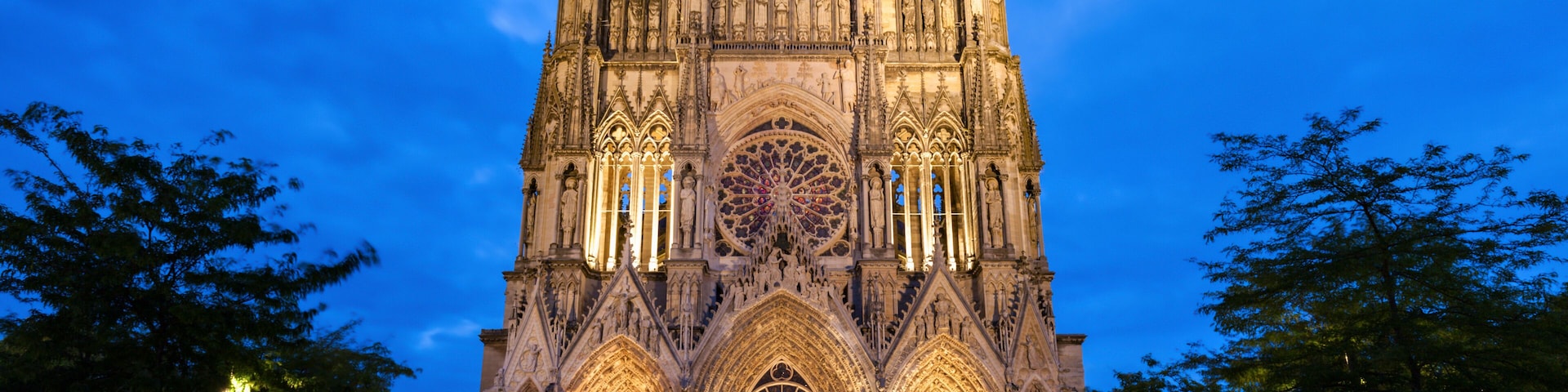 Una catedral gótica con dos torres gemelas, un gran rosetón y un patio con zonas de estar.