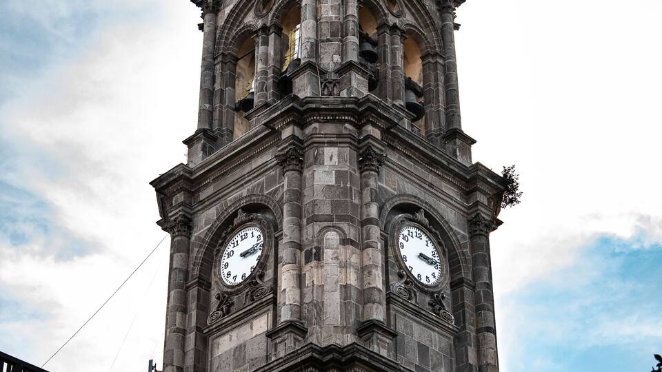 A tall clock tower with two large clocks on each side, set against a partly cloudy sky.