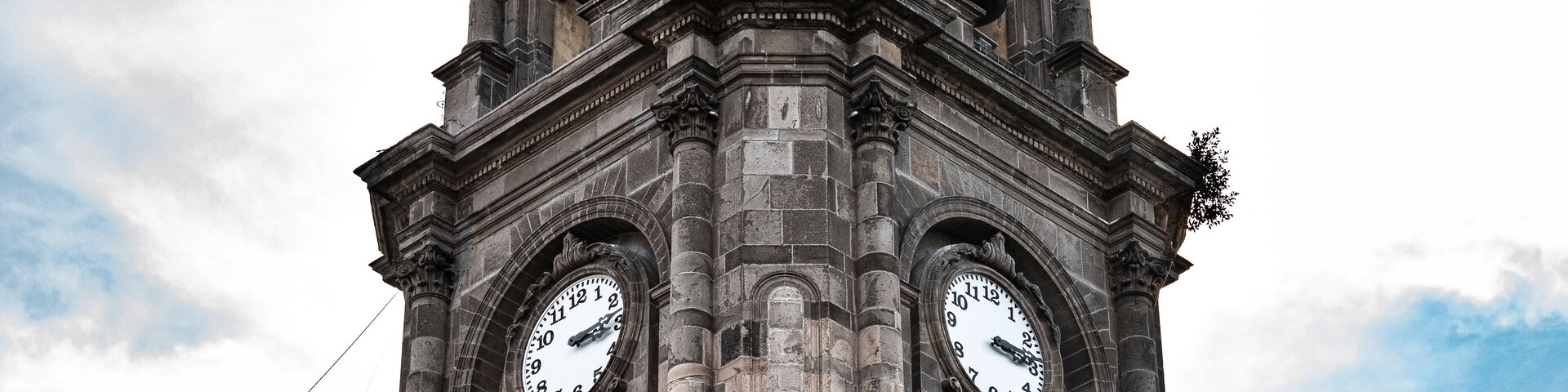 Una alta torre del reloj con dos grandes relojes a cada lado, sobre un cielo parcialmente nublado.
