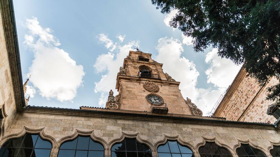 A historic building with a clock tower, arched windows, and a clear sky with clouds.
