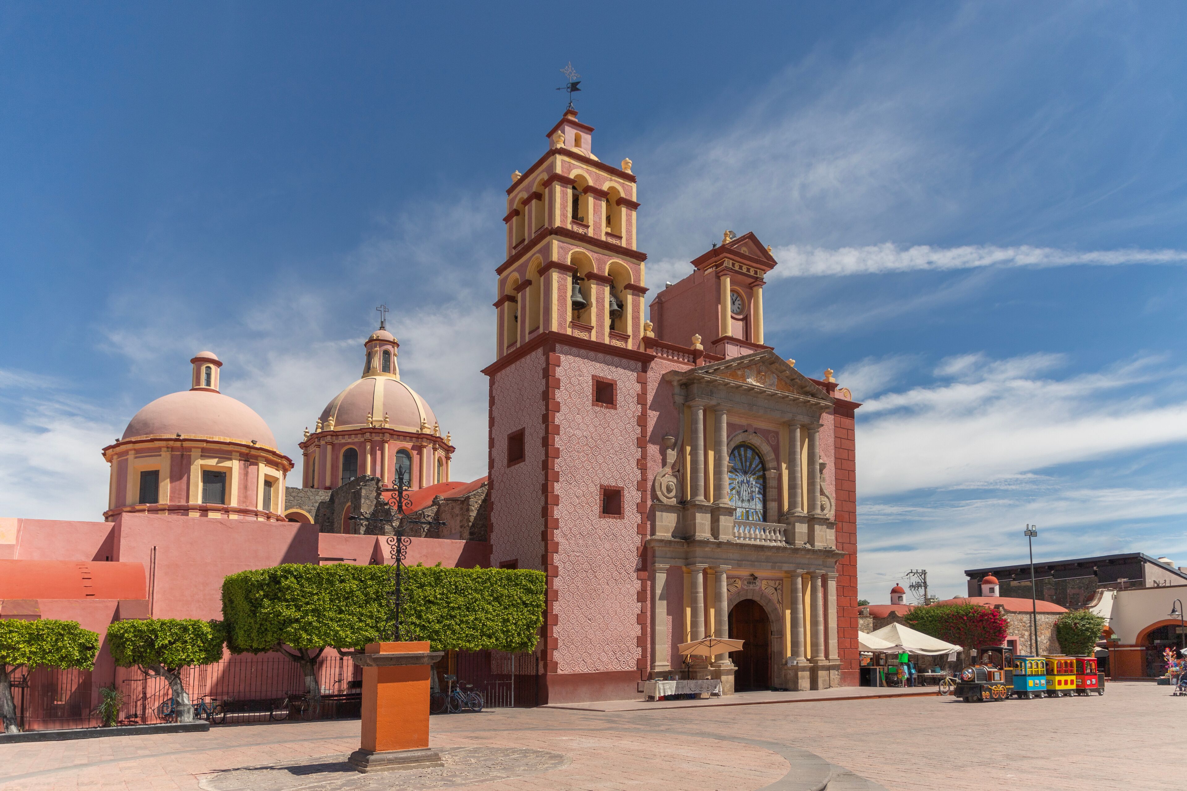 Una iglesia histórica con un campanario y cúpulas, rodeada por una plaza con un tren pequeño y puestos de mercado.
