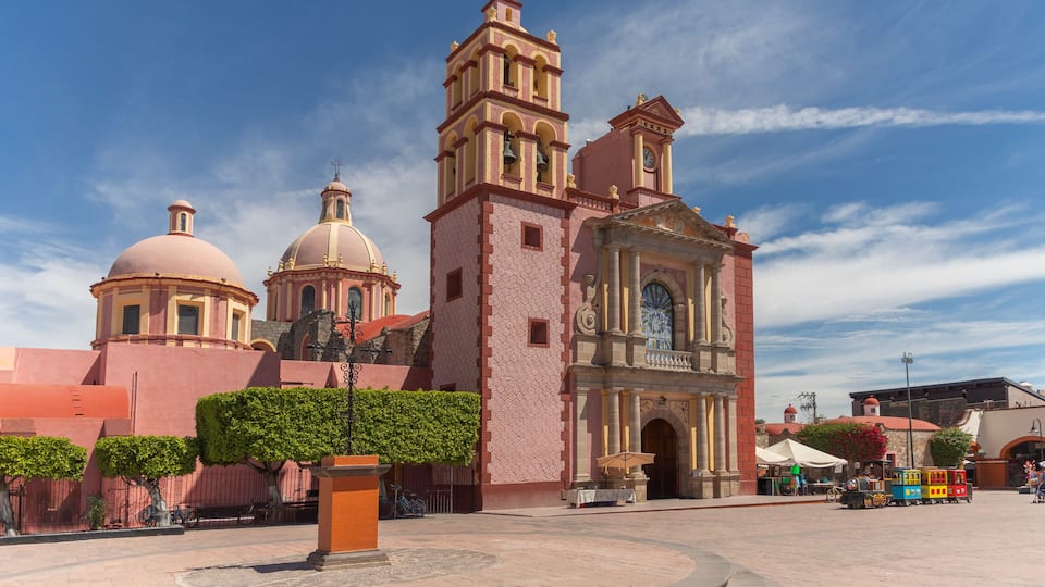 A historic church with a bell tower and domes, surrounded by a plaza with a small train and market stalls.