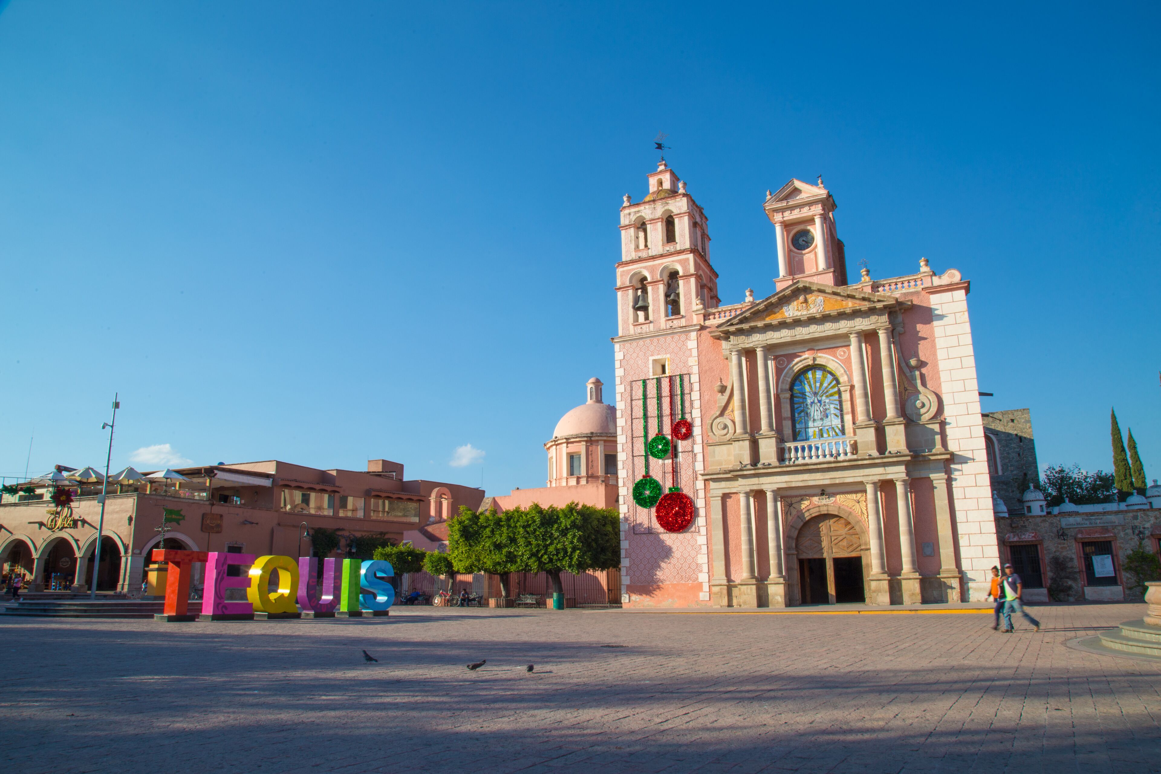 A historic church with a bell tower and a plaza with colorful letters spelling 'TEQUIS'.