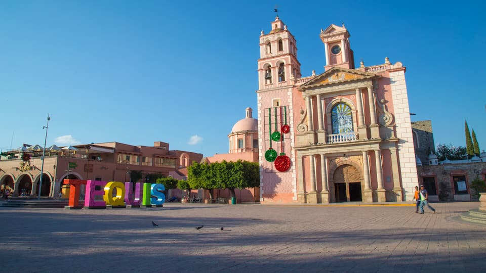 A historic church with a bell tower and a plaza with colorful letters spelling 'TEQUIS'.
