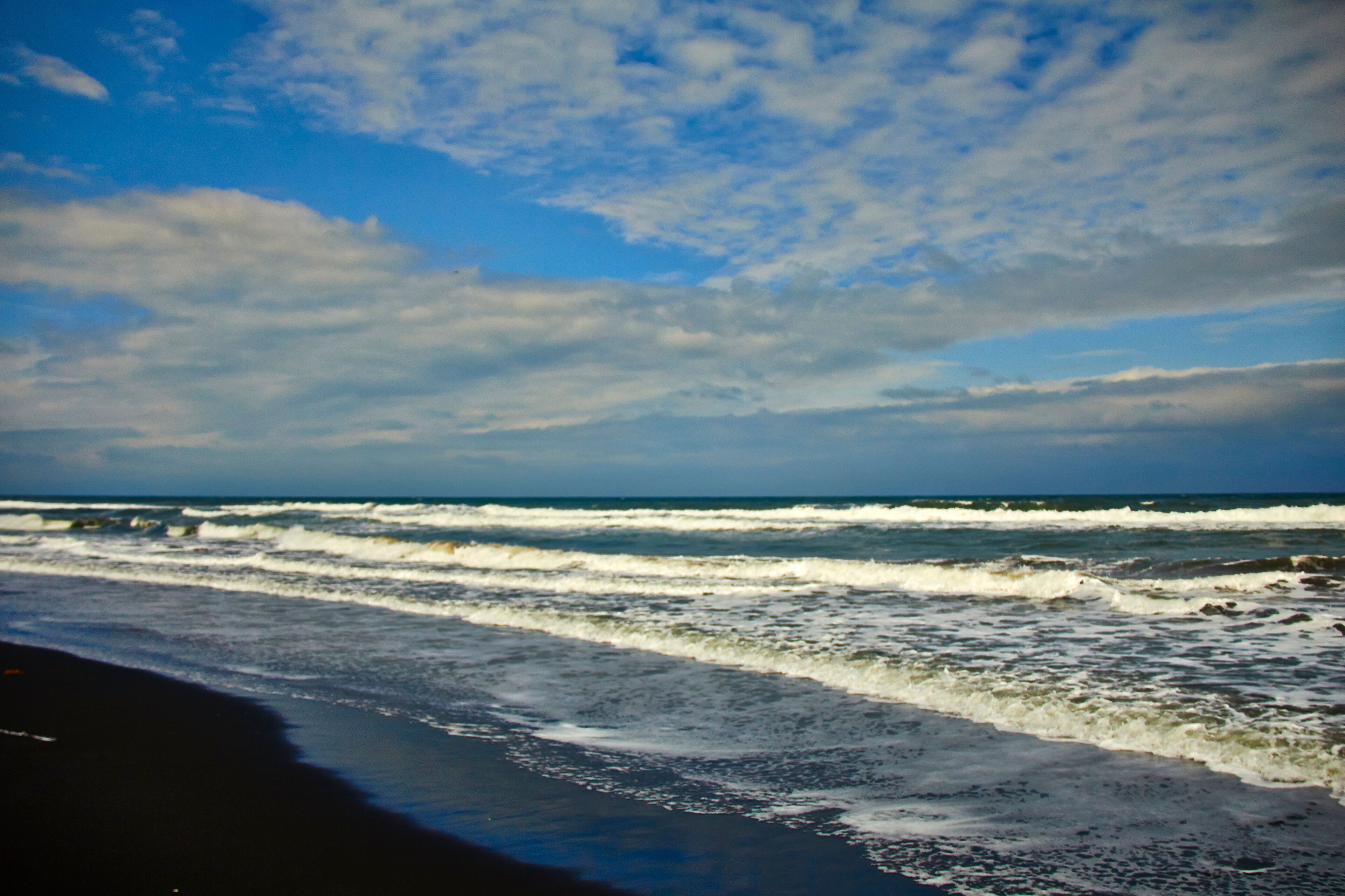 A beach with waves crashing onto the shore under a partly cloudy sky.