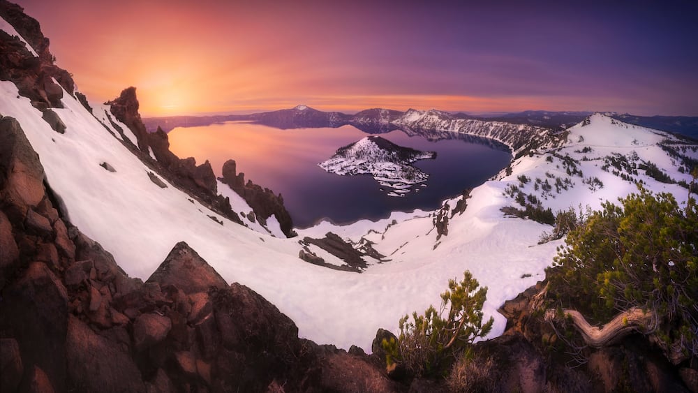View of Crater Lake at sunset with snow-covered mountains and a serene reflection, Chiloquin, Oregon, United States.
