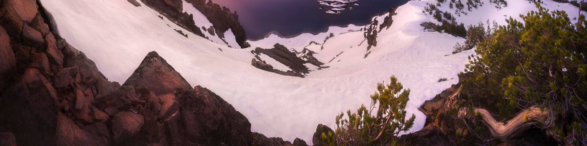View of Crater Lake at sunset with snow-covered mountains and a serene reflection, Chiloquin, Oregon, United States.