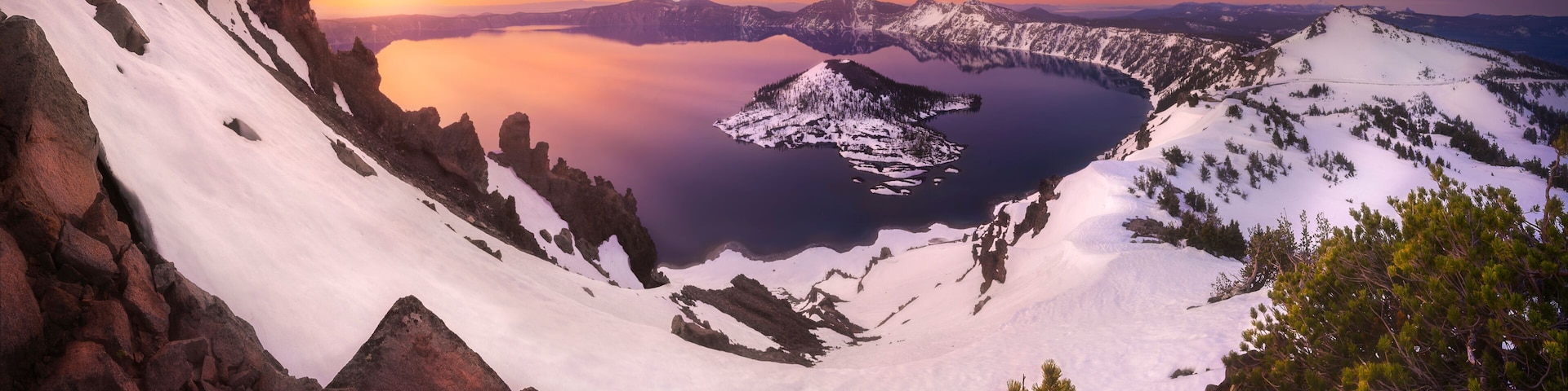 View of Crater Lake at sunset with snow-covered mountains and a serene reflection, Chiloquin, Oregon, United States.