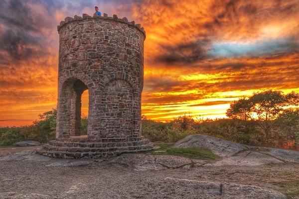 A stone tower with an arched entrance, set against a sunset sky with clouds.