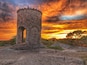 A stone tower with an arched entrance, set against a sunset sky with clouds.