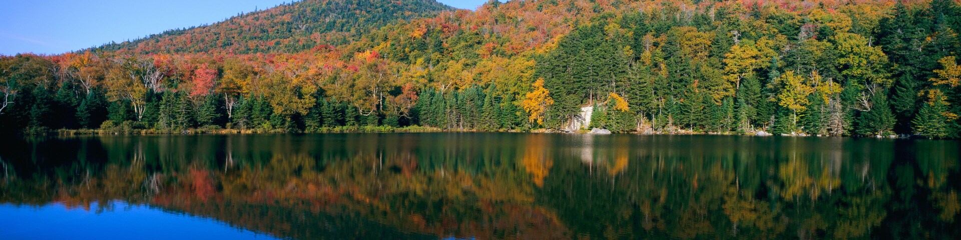 Um lago calmo refletindo uma floresta com folhagem outonal.