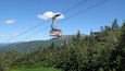 Une télécabine portant l’inscription « Cannon », suspendue à un câble, avec un paysage montagneux et une forêt dense en arrière-plan.
