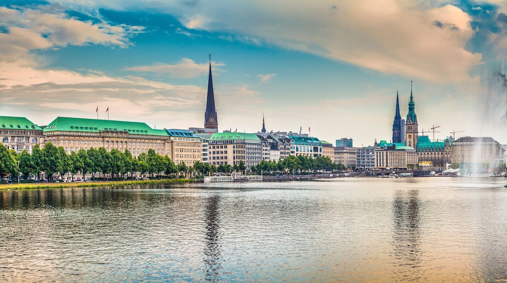 A cityscape with a prominent church steeple, a fountain, and a river reflecting the buildings.