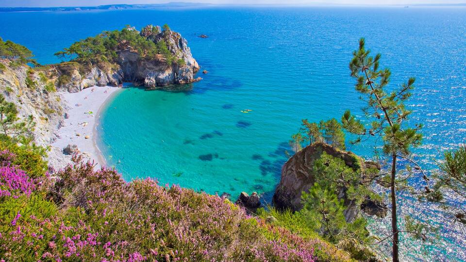 A coastal landscape with a turquoise beach, rocky cliffs, and dense vegetation.