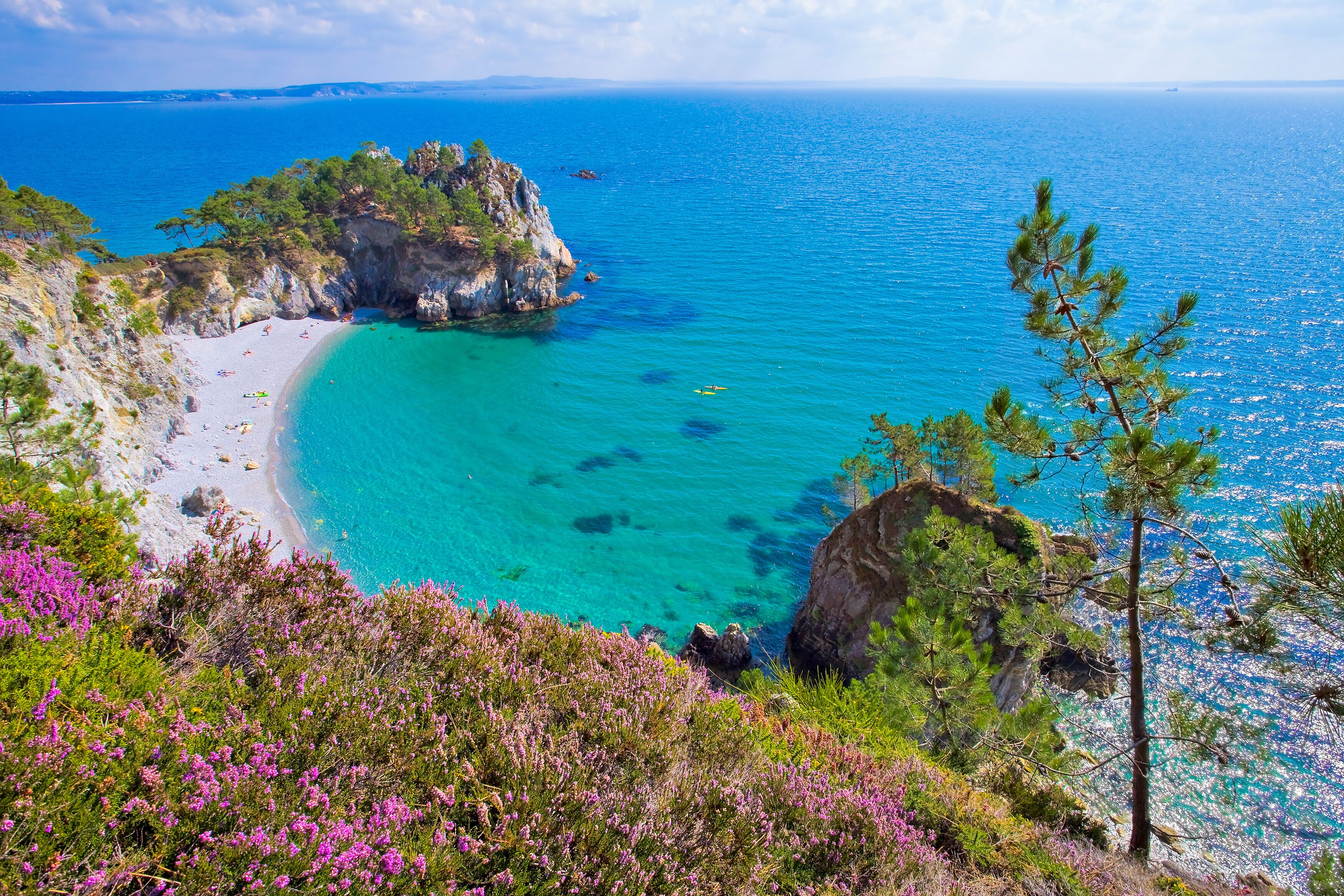 A coastal landscape with a turquoise beach, rocky cliffs, and dense vegetation.