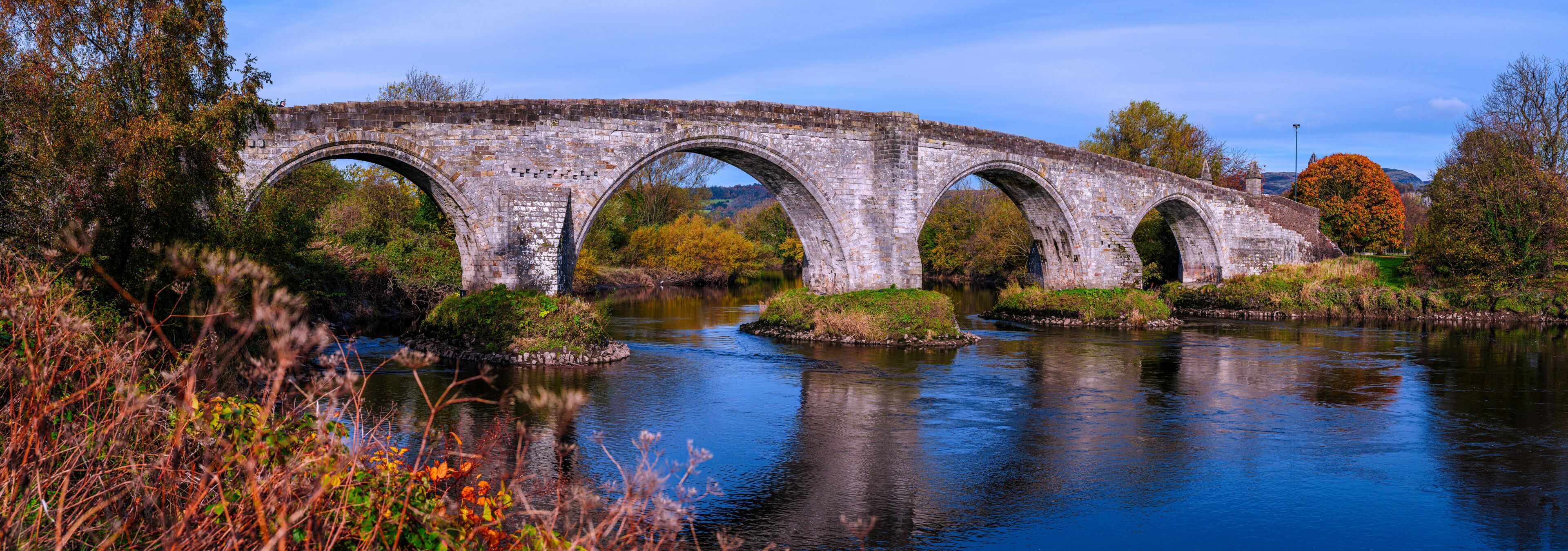A stone bridge over a river with autumn foliage.