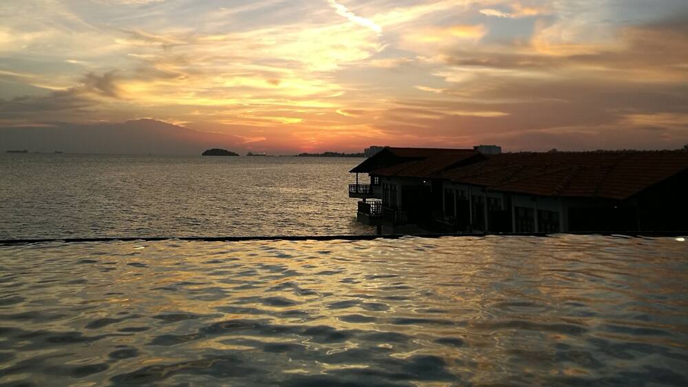 A sunset over a calm sea with a pier and buildings in the foreground.