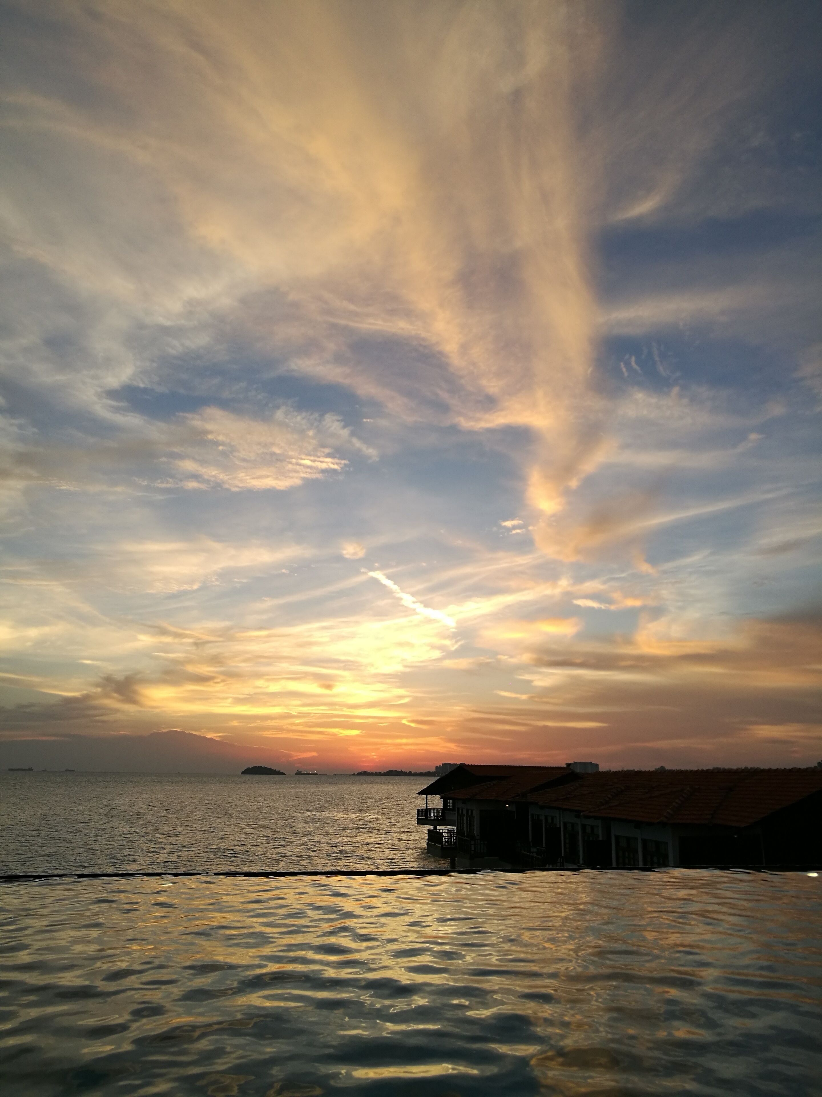 A sunset over a calm sea with a pier and buildings in the foreground.