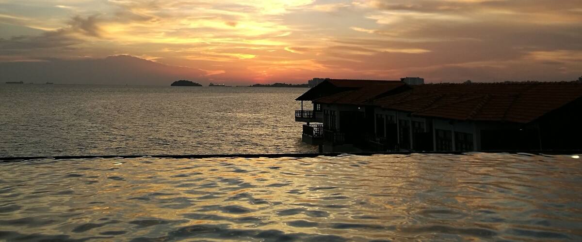 A sunset over a calm sea with a pier and buildings in the foreground.
