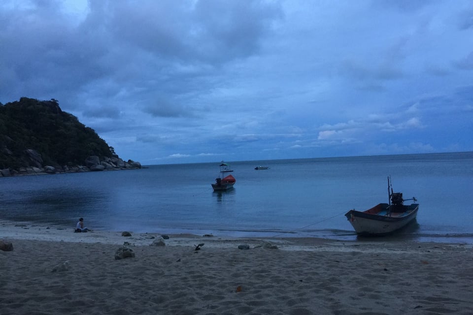 En strand med båtar, en klippig ö och en molnig himmel.