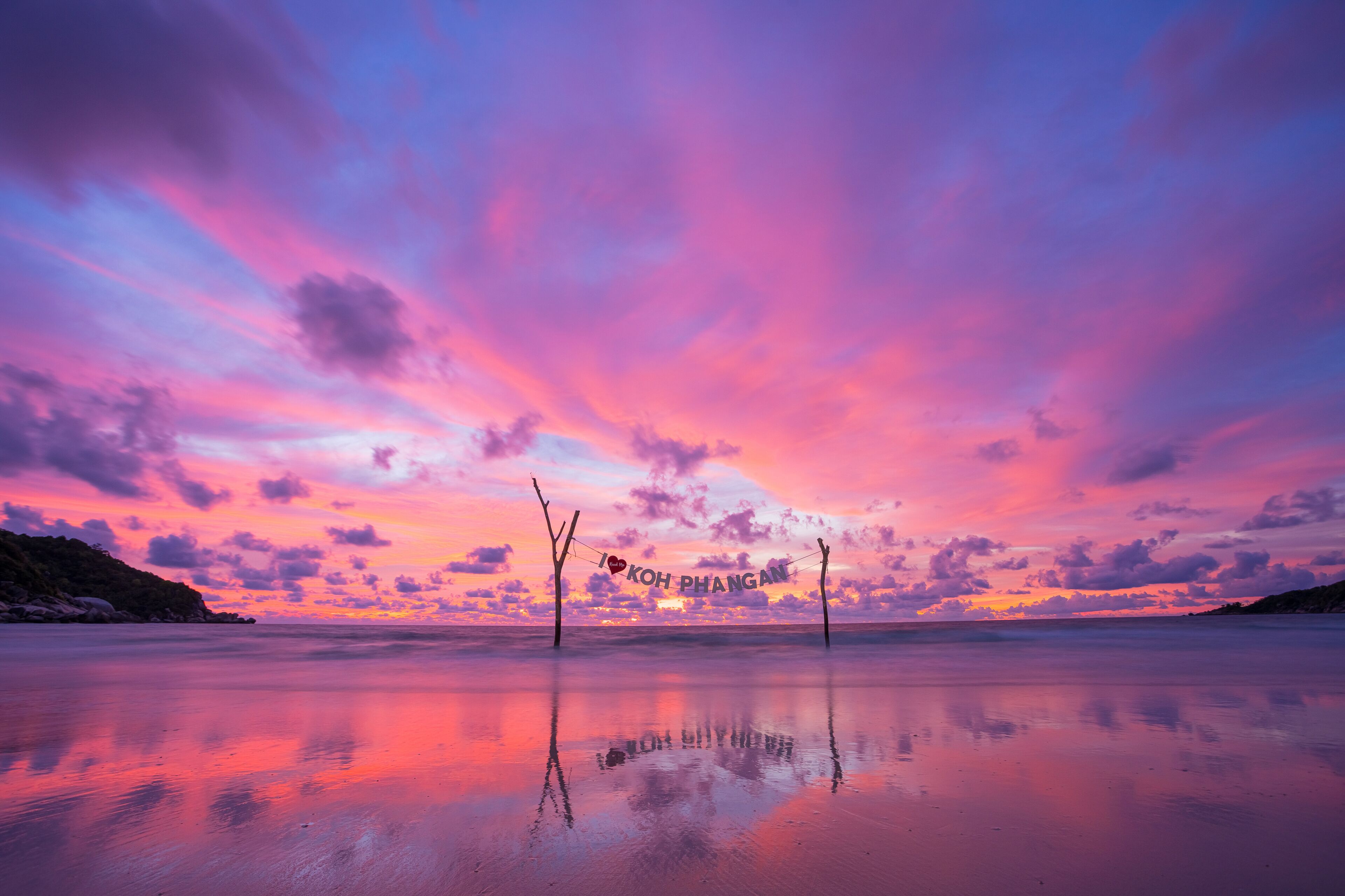 Una playa al atardecer con un cielo en tonos rosados y morados, y un reflejo sobre la arena mojada.