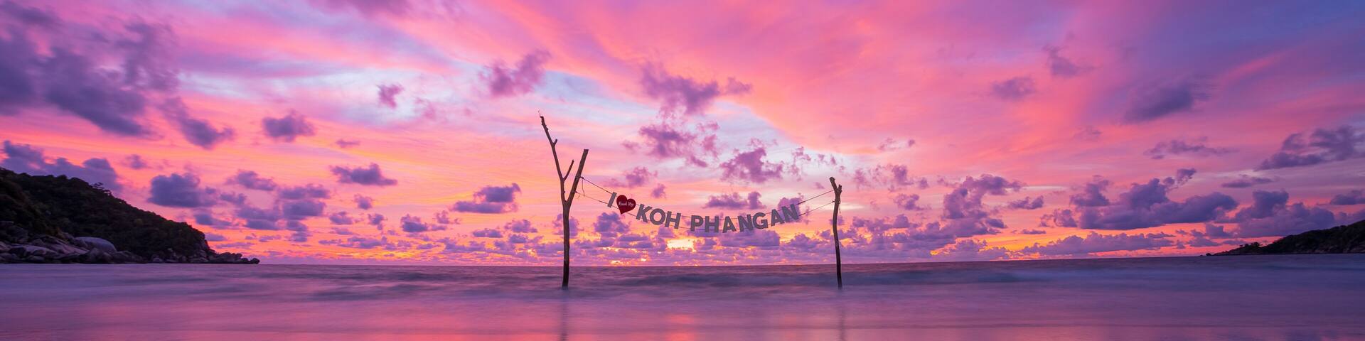 A beach at sunset with a sky in shades of pink and purple, and a reflection on the wet sand.