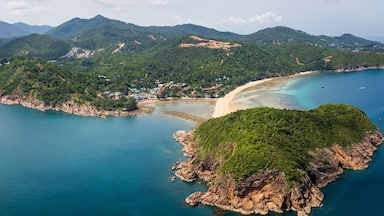 Vista aérea de uma área costeira com praia arenosa, águas turquesa cristalinas e colinas verdejantes.