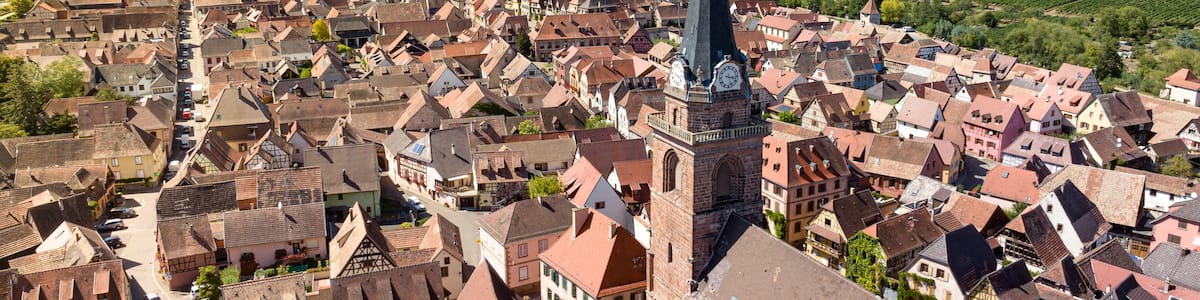 A town with a prominent church tower, surrounded by vineyards and rolling hills.