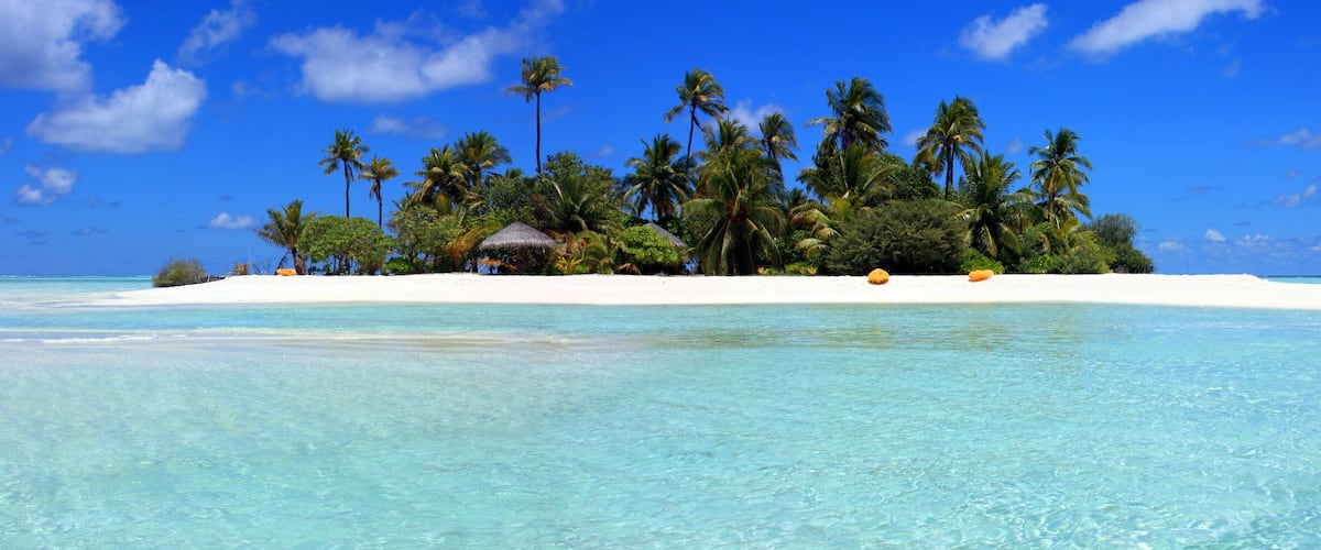 A tropical island with clear turquoise waters, white sand, and lush palm trees.