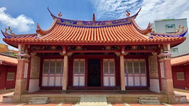 Un edificio tradicional chino con tejas ornamentales rojas y azules, una entrada central y estatuas decorativas de leones en el techo.