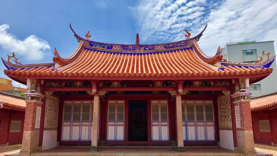 A traditional Chinese building with ornate red and blue roof tiles, a central entrance, and decorative lion statues on the roof.