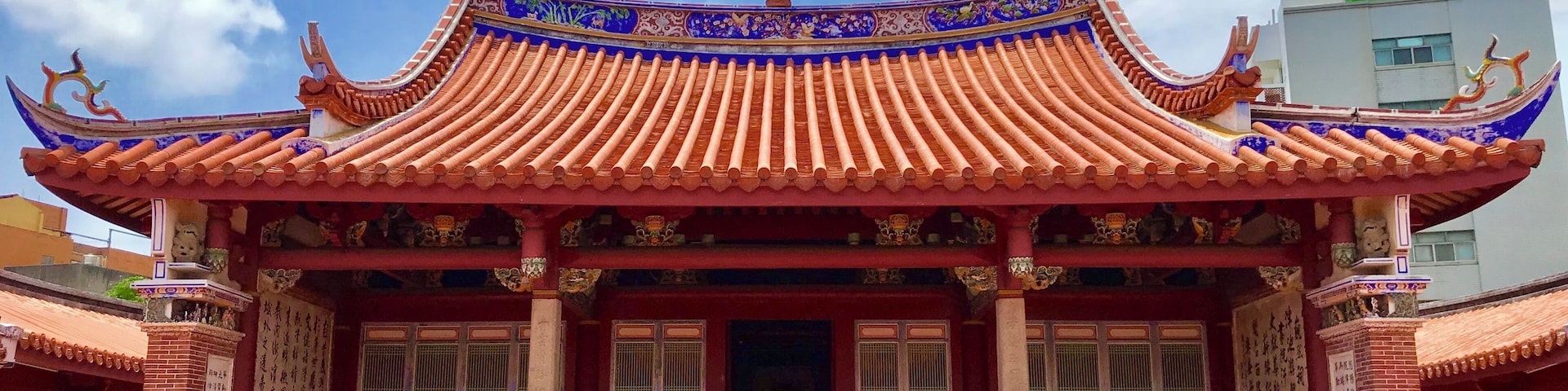 Un edificio tradicional chino con tejas ornamentales rojas y azules, una entrada central y estatuas decorativas de leones en el techo.