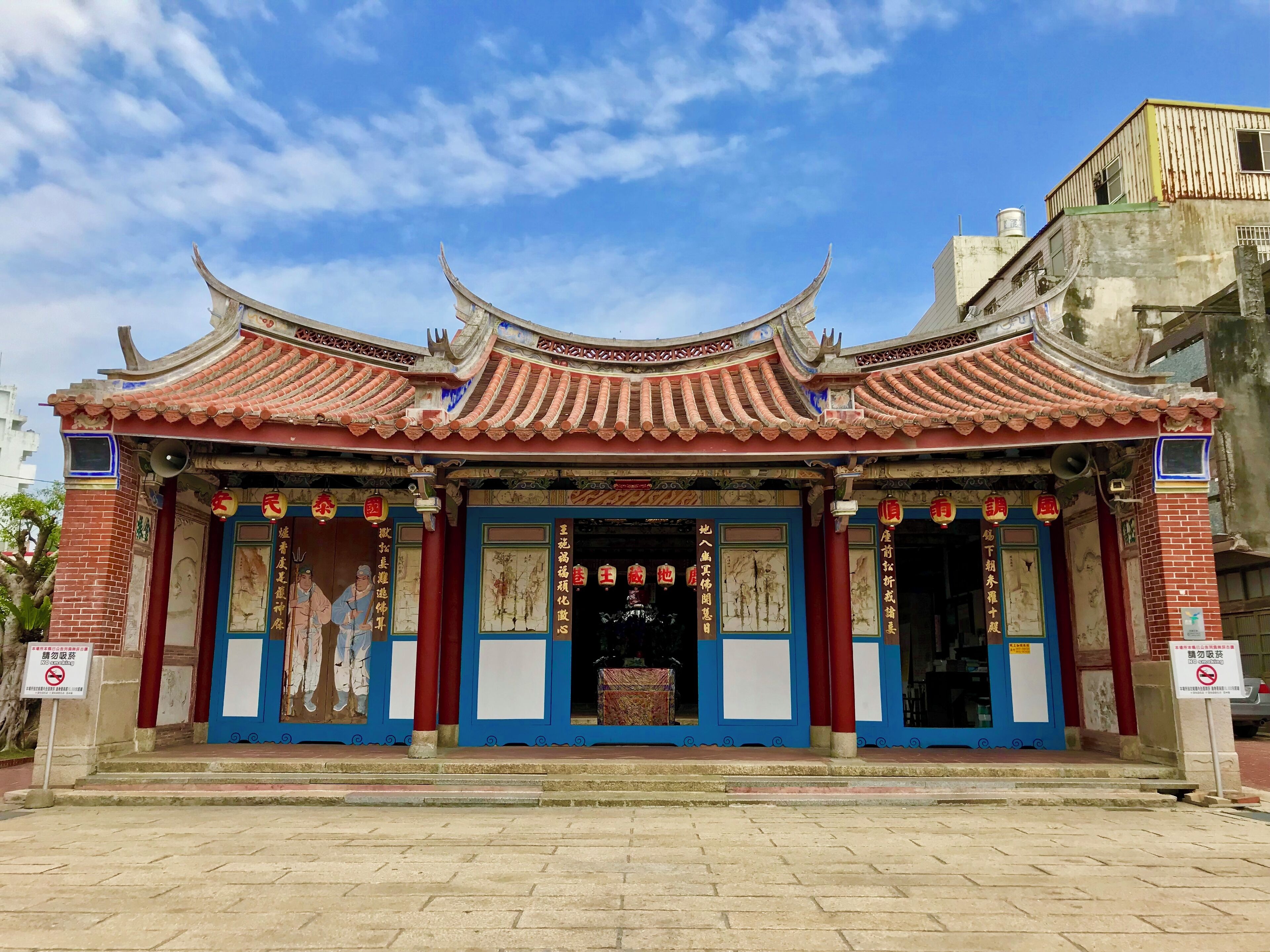 A traditional Chinese temple with ornate red and blue roof tiles, red pillars, and detailed wall paintings.