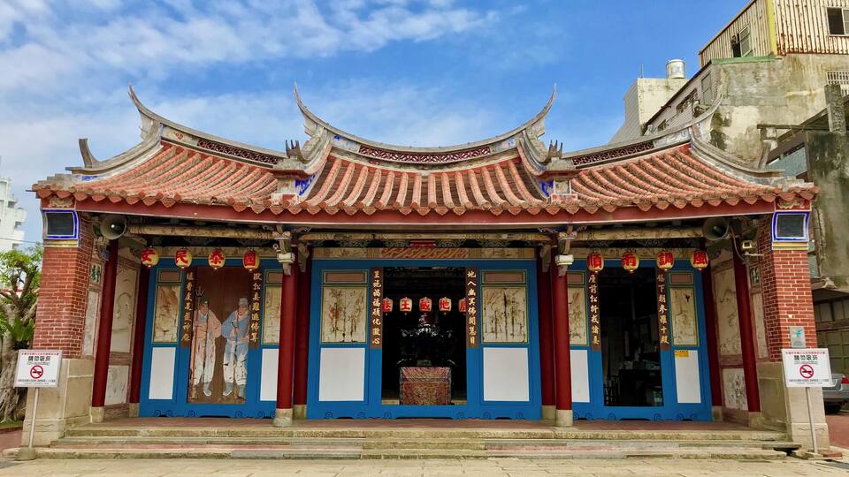 A traditional Chinese temple with ornate red and blue roof tiles, red pillars, and detailed wall paintings.