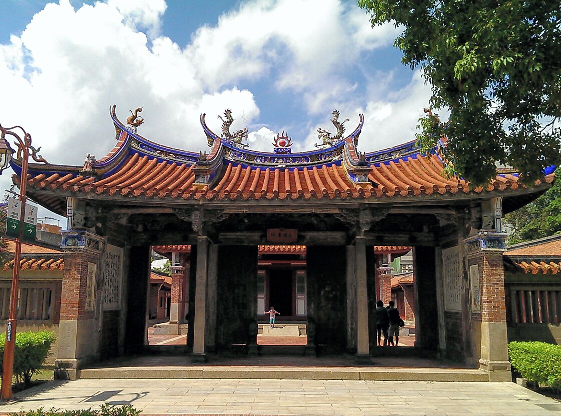 Un portón tradicional chino con tejas azules y doradas muy ornamentadas y decoraciones de dragones.