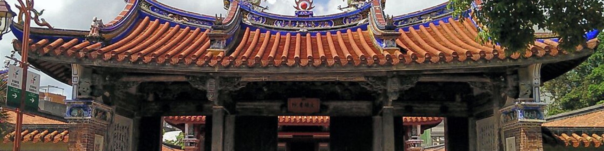 Un portón tradicional chino con tejas azules y doradas muy ornamentadas y decoraciones de dragones.