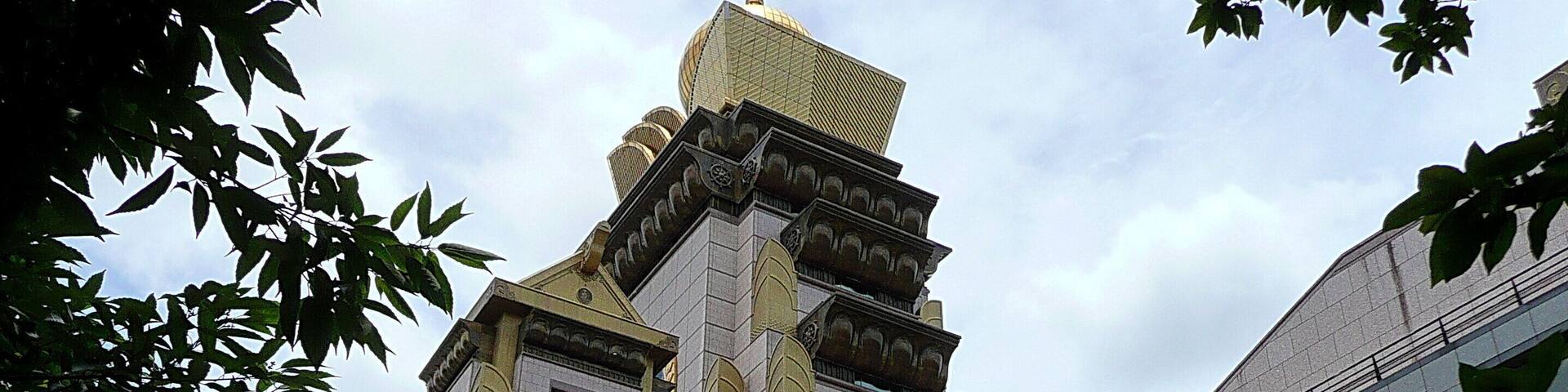 A historic building with a golden dome and intricate architecture, surrounded by modern buildings and lush greenery.