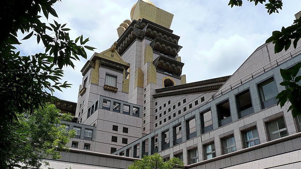 A historic building with a golden dome and intricate architecture, surrounded by modern buildings and lush greenery.