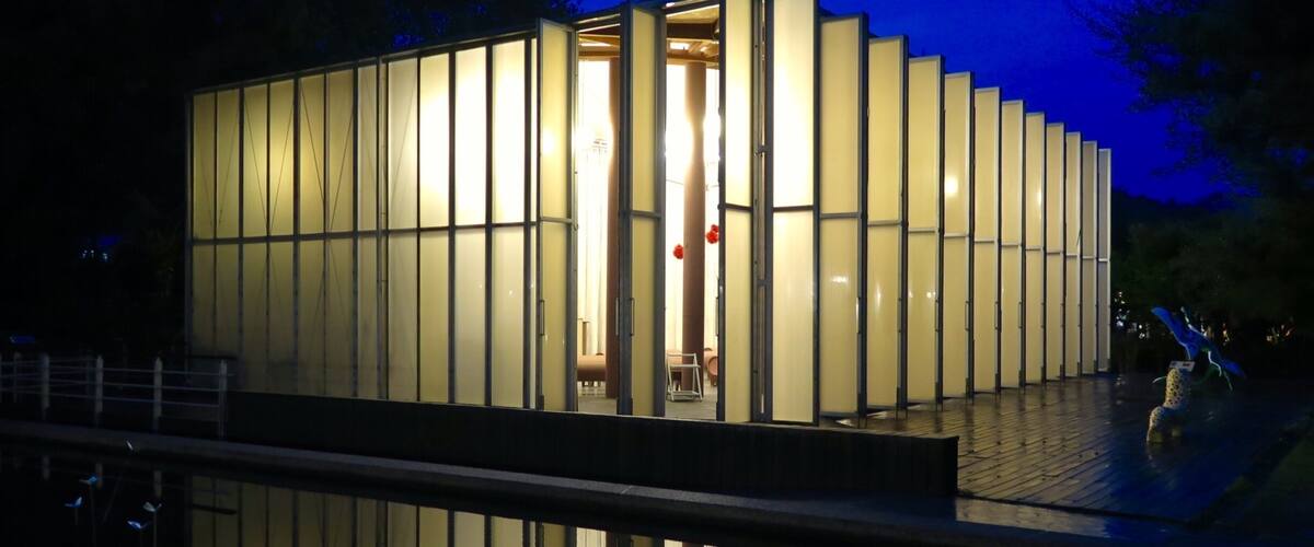 A modern building with vertical glass panels and a reflection in the water.