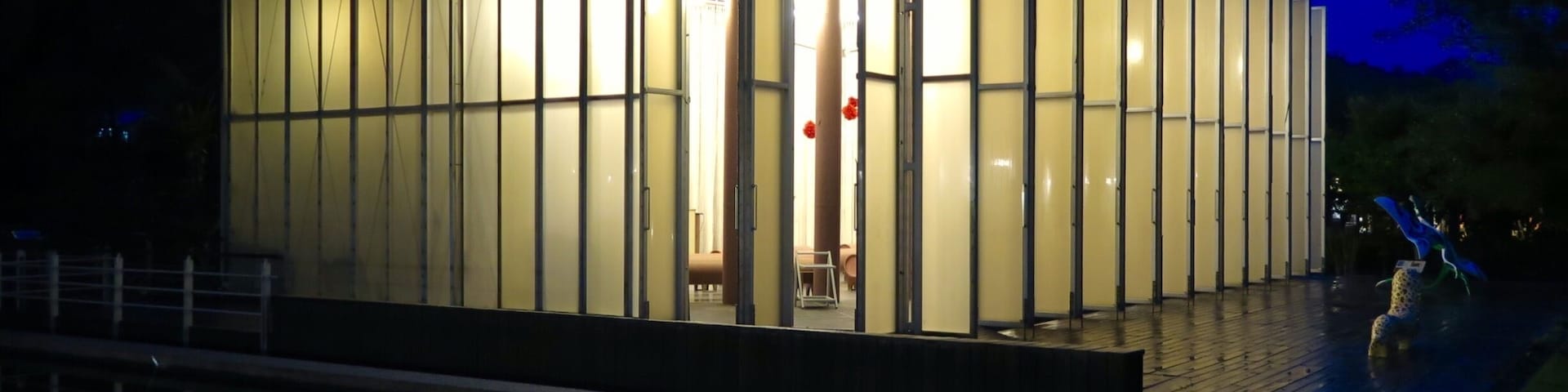 Un edificio moderno con paneles de vidrio verticales y un reflejo en el agua.