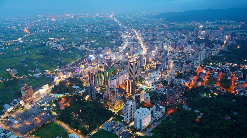 An aerial view of a cityscape at dusk with illuminated buildings and roads.