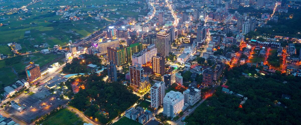 An aerial view of a cityscape at dusk with illuminated buildings and roads.