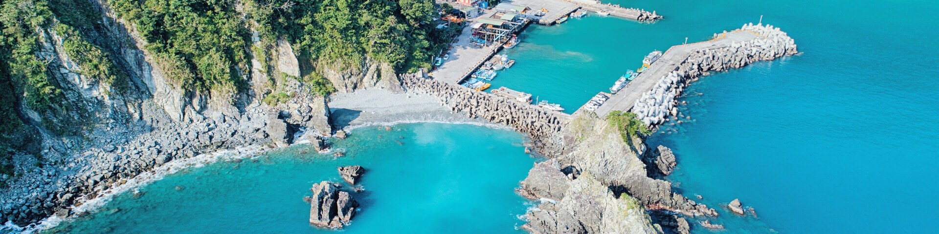 Un paisaje costero con mar turquesa transparente, afloramientos rocosos y una ladera cubierta de bosque.
