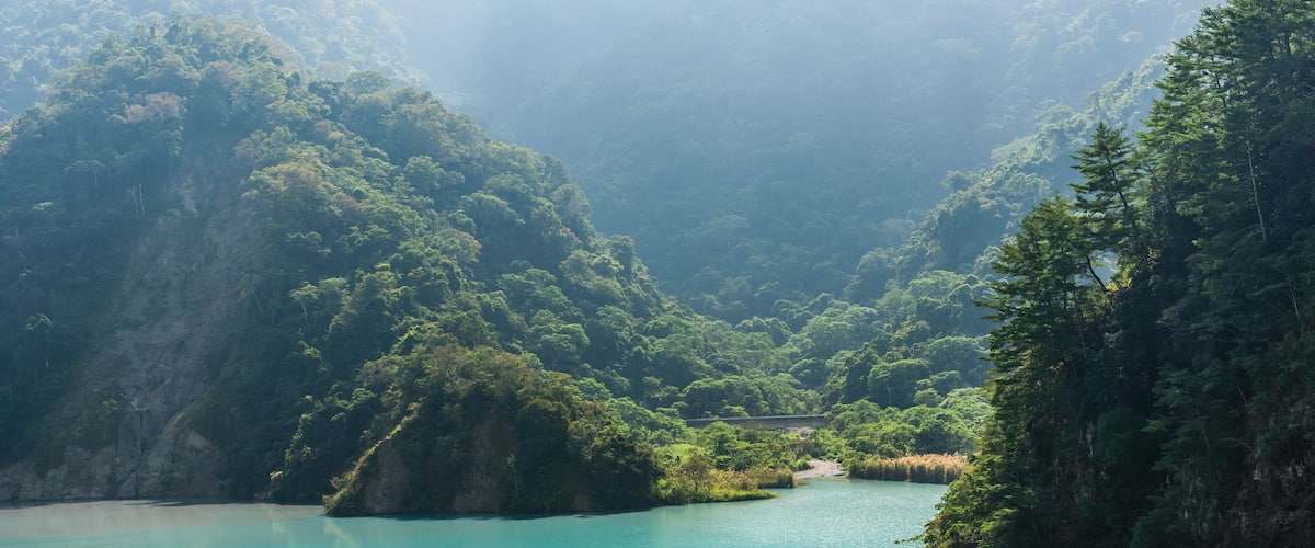 A turquoise lake surrounded by lush green hills and dense forest.