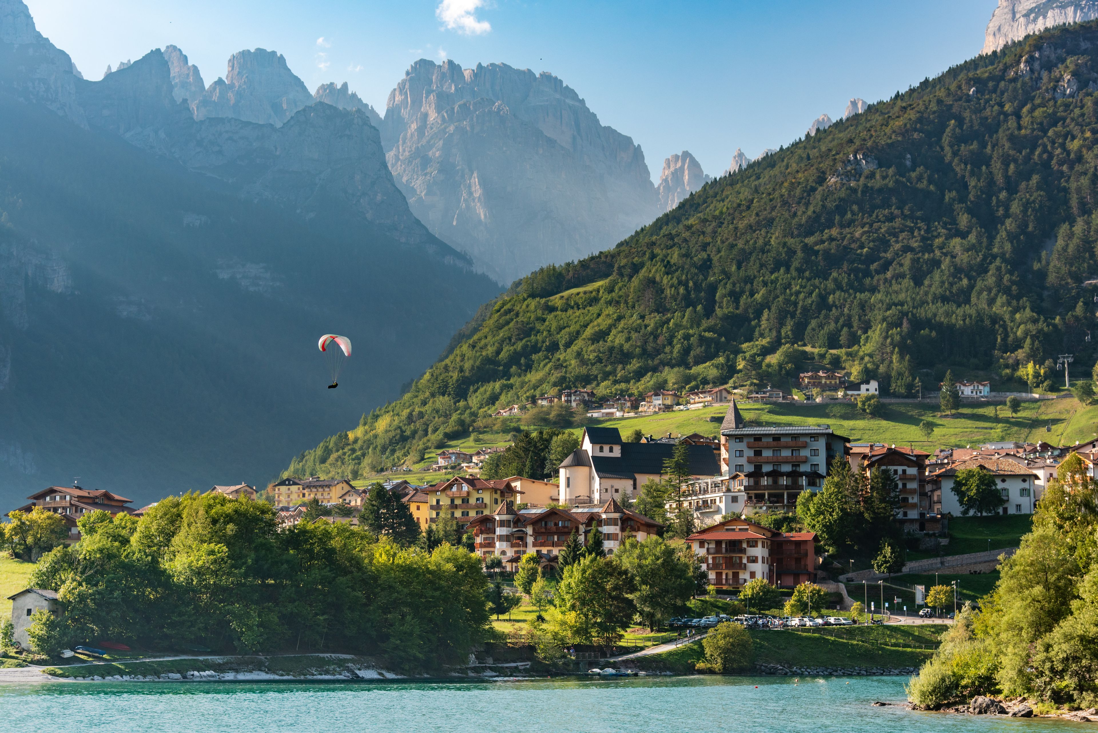 A mountainous landscape with a lake, a town with traditional buildings, and a paraglider in the distance.